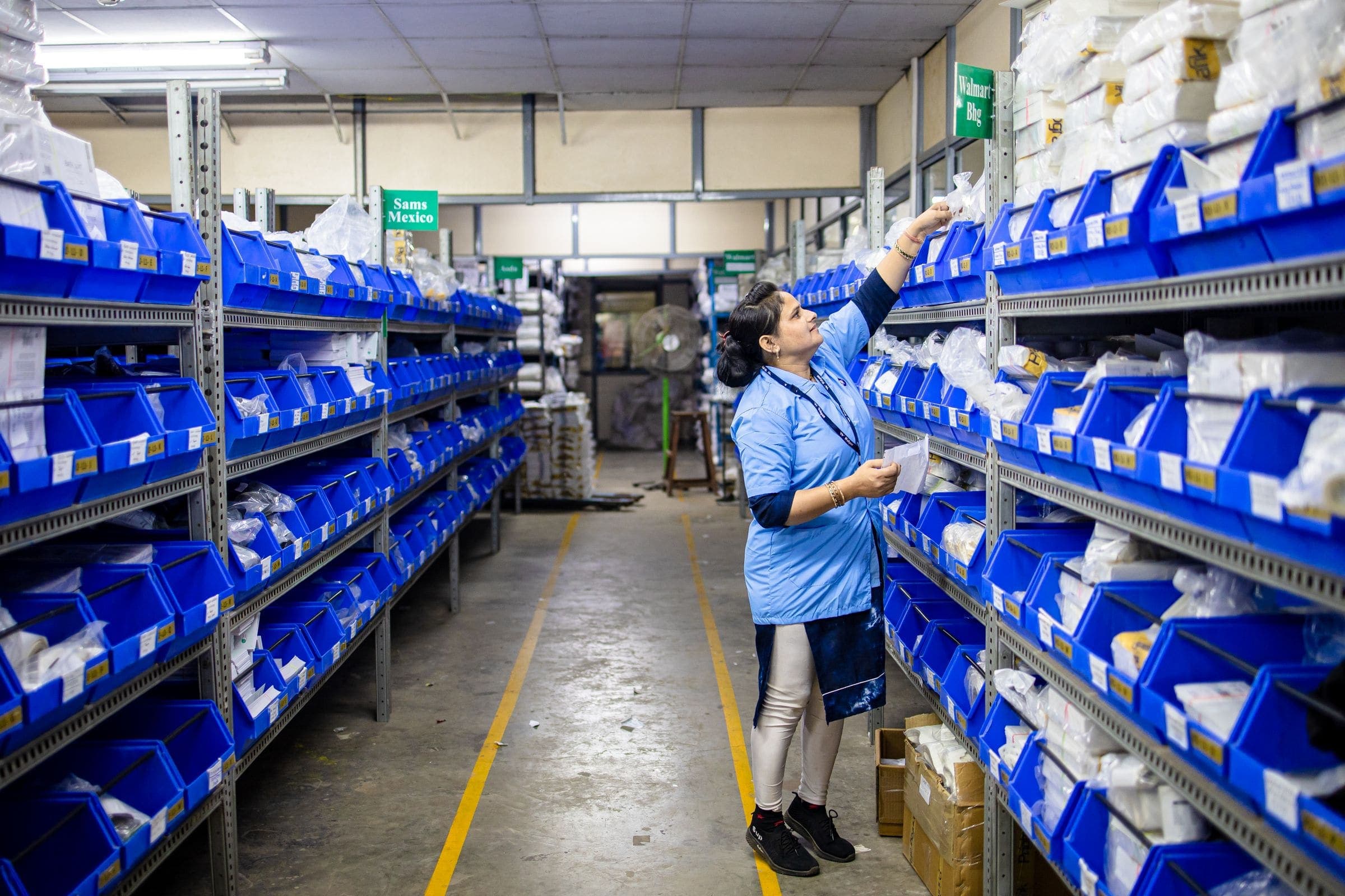Warehouse worker checking stock in rows of labelled blue storage bins