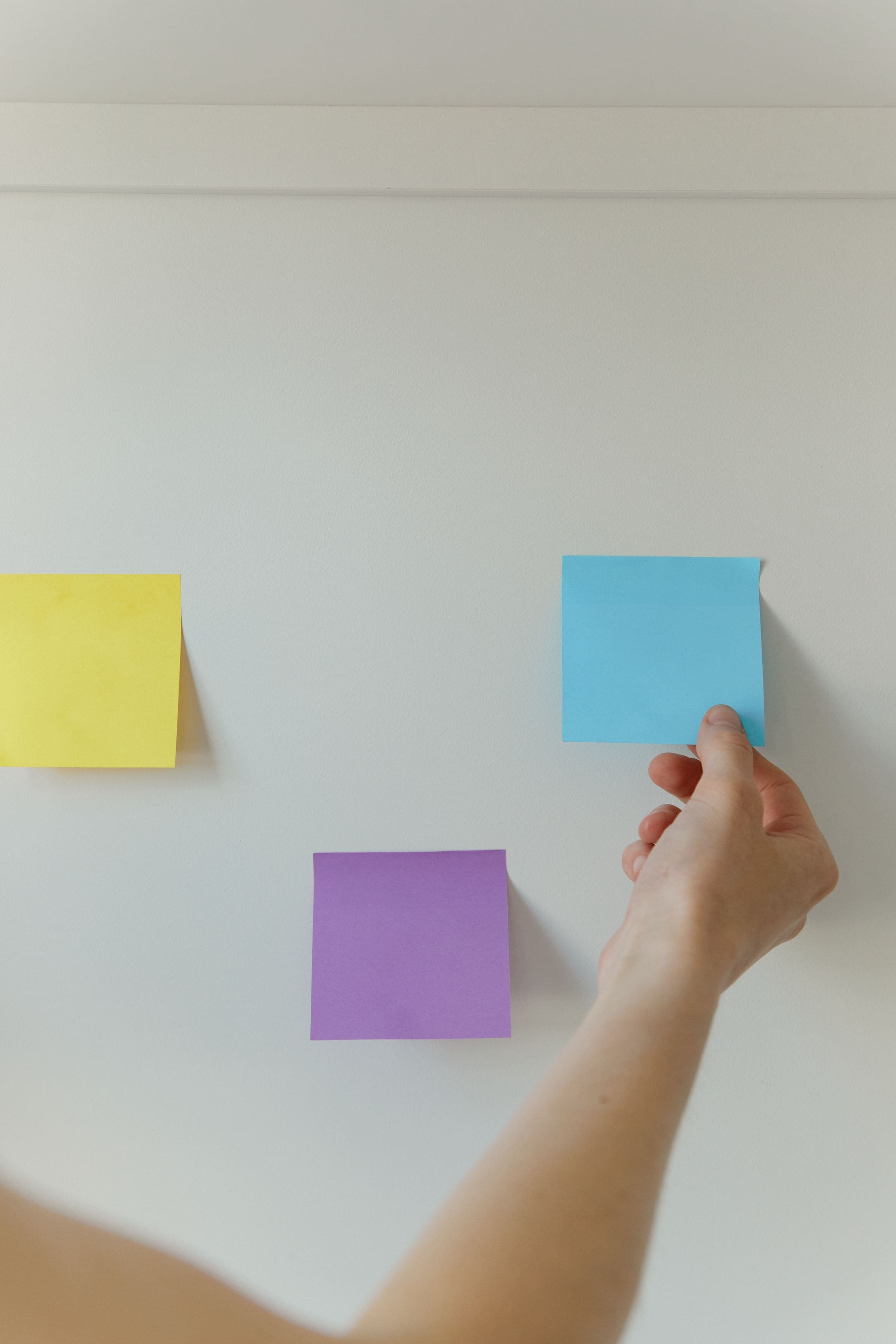 A hand placing coloured sticky notes on a wall while mapping a process